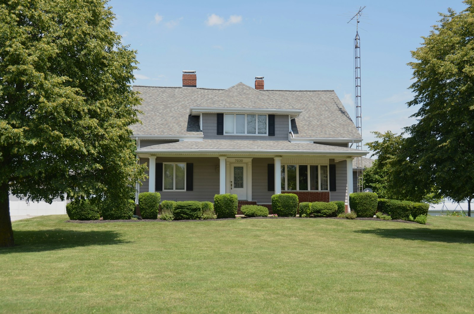 Traditional grey house with a porch green lawn and trees